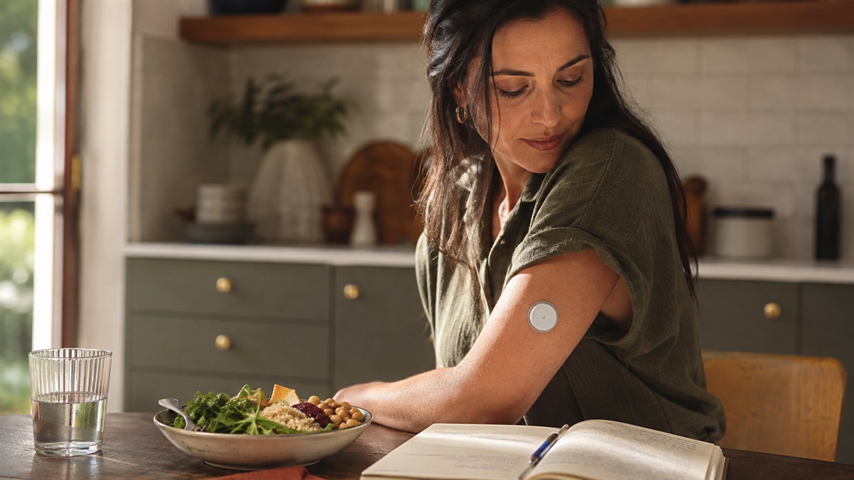 An adult with an upper-arm glucose sensor at a kitchen table.